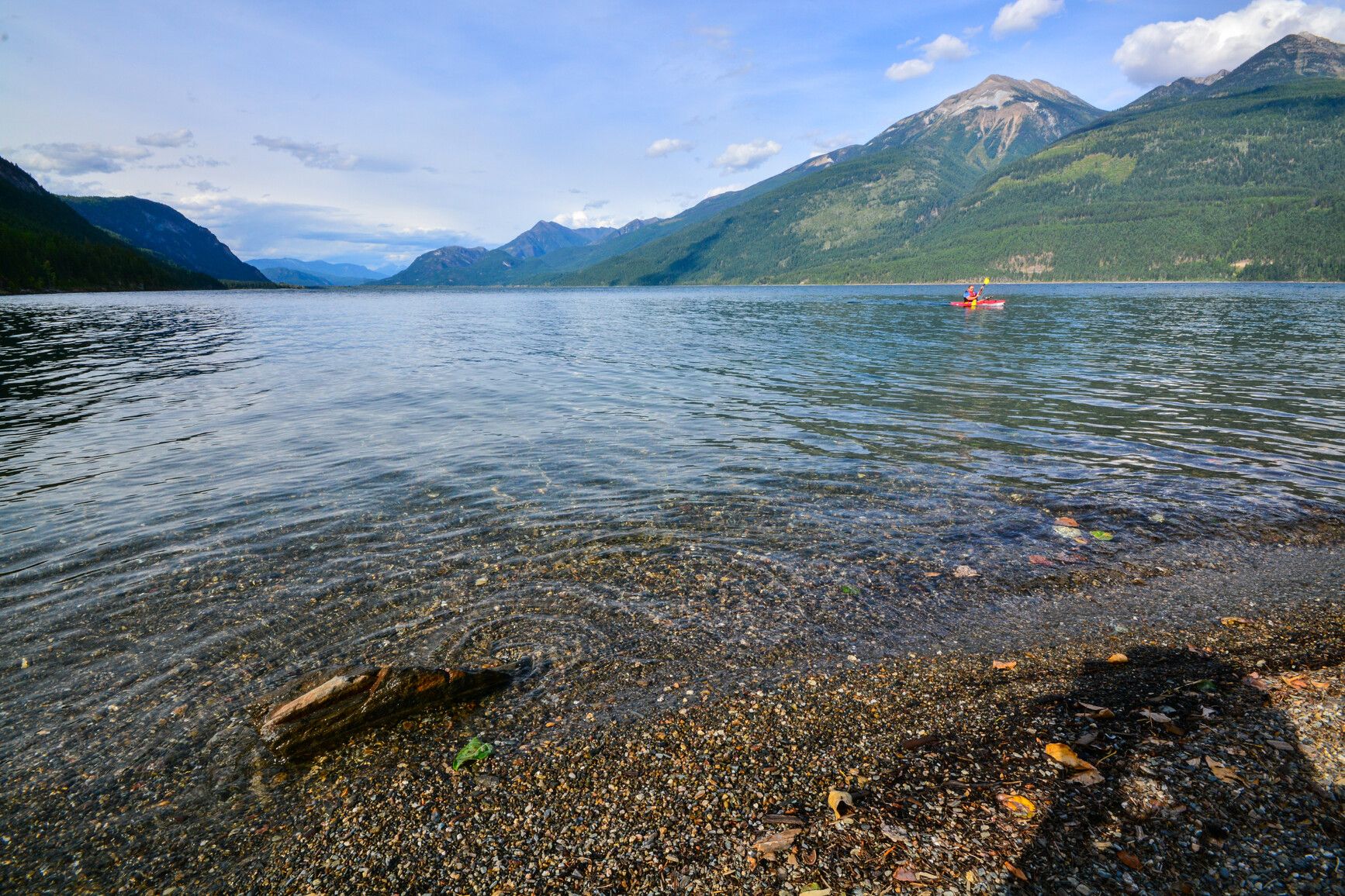 Mountains surround the lake as a kayaker paddles along at Kootenay Lake Park.