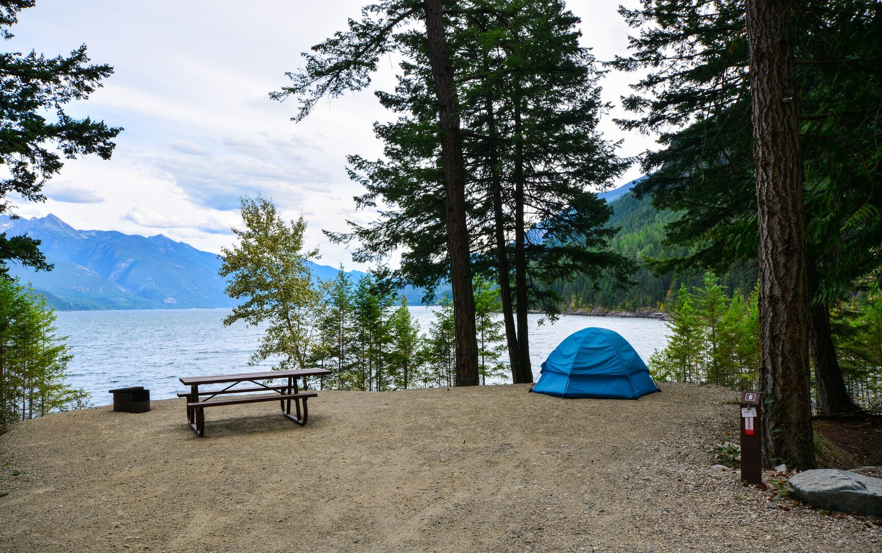 A lakeside campsite with a tent, set against the backdrop of forest-covered mountains at Kootenay Lake Park. A perfect spot to unwind and relax.
