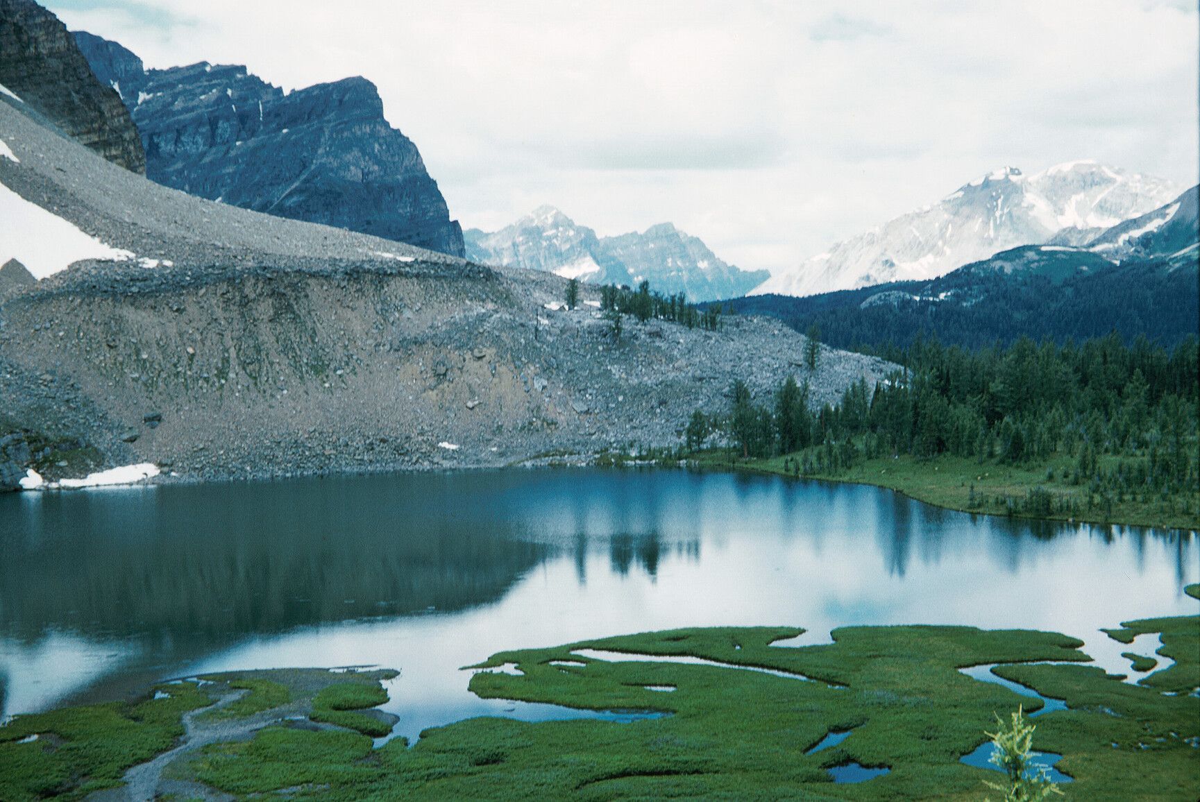 A proglacial lake in Mount Assiniboine Park, bordered by a steep moraine ridge, reflects the rugged peaks rising beyond.