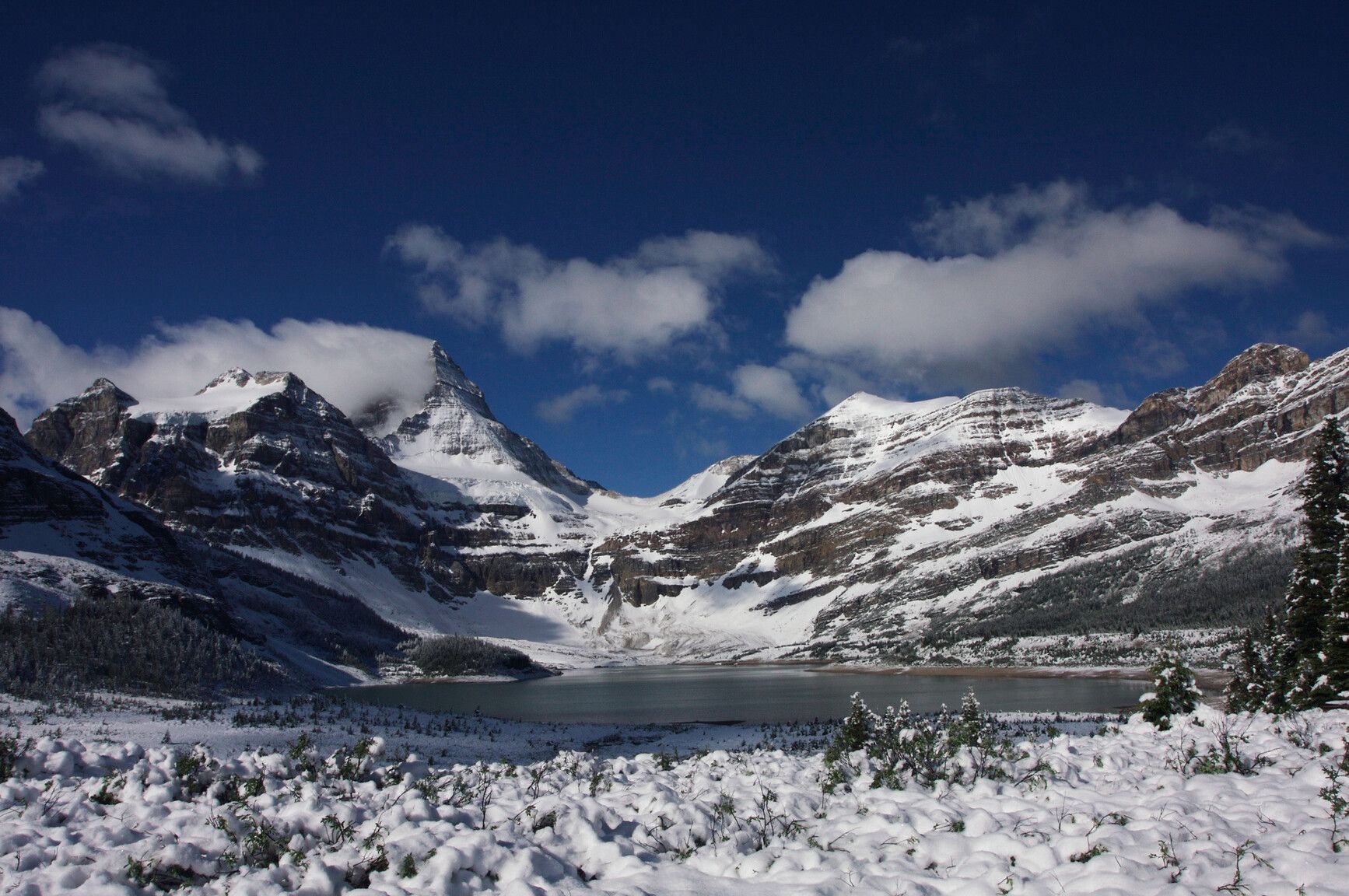 Winter stillness in Mount Assiniboine Park. A high-elevation tarn lies frozen beneath snow-laden peaks, marking the seasonal shift from glacial melt to icy dormancy. The lake’s basin, carved by ancient ice, mirrors the crisp clarity of alpine skies.