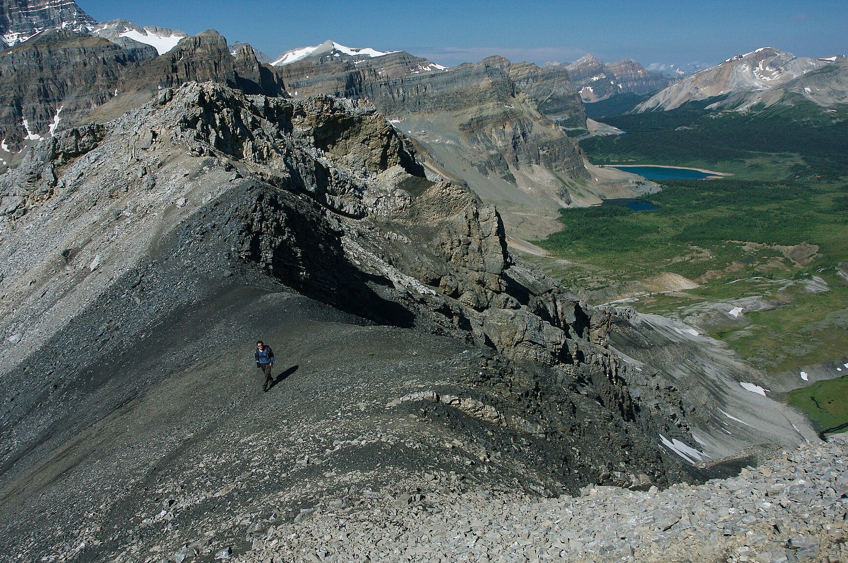 A hiker walks a mountain ridge high above a green valley in Mount Assiniboine Park.