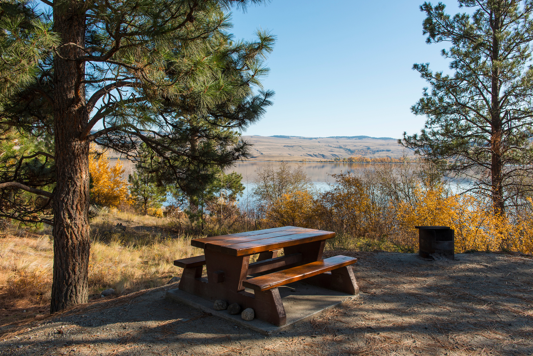 Vacant campsite with lake and grassy rolling hills view.