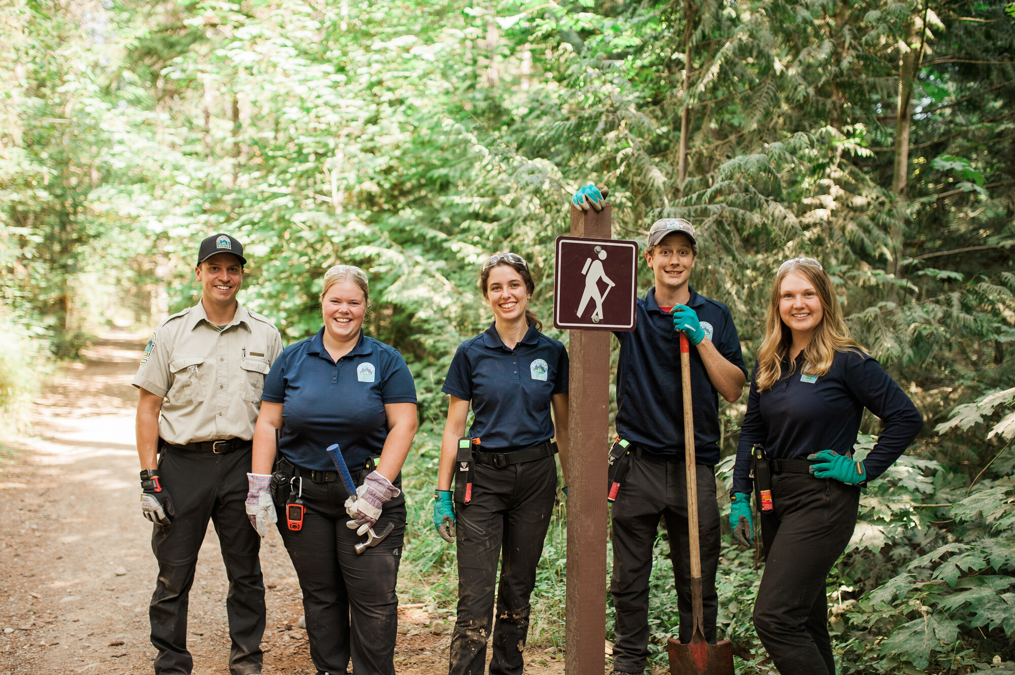 (Student) Rangers posing beside a new hiking trail sign they installed