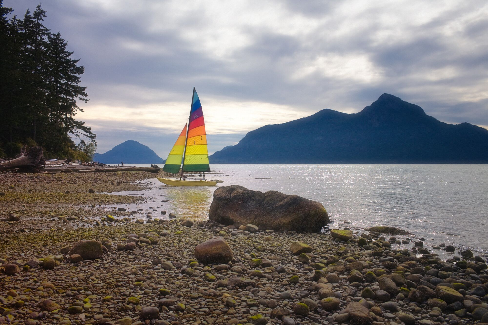 A boat with colourful sails rests on the edge of the shore. Porteau Cove Park.