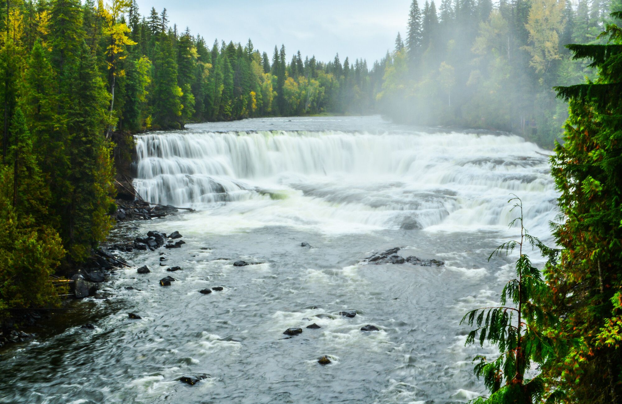 Mist rises above the cascading waters of the horseshoe shape of Dawson Falls in the fall. Wells Gray Park.