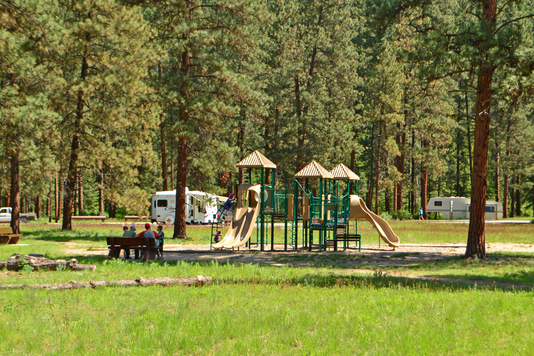 People sitting on picnic table near playground. Campsites with RV's in background.