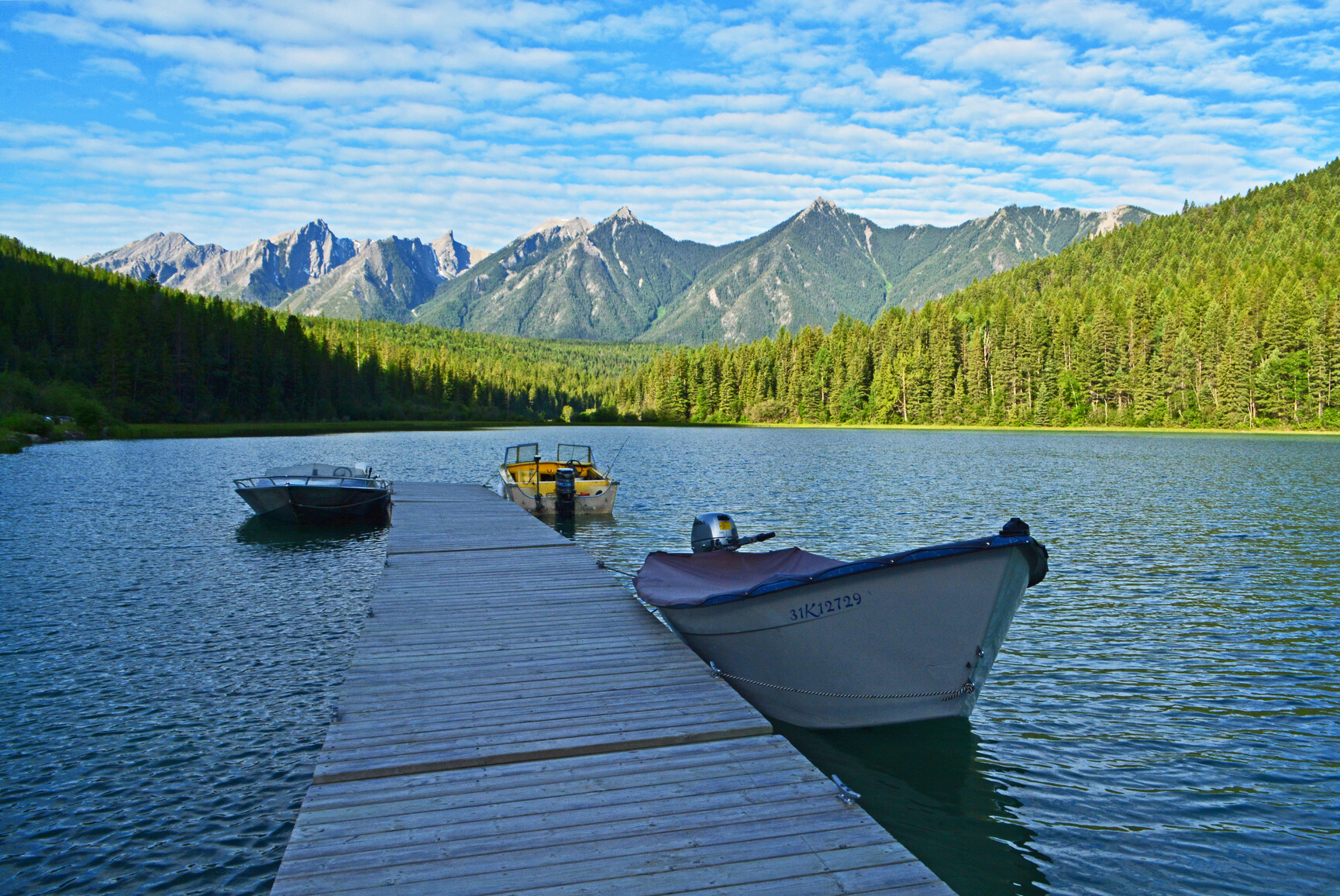Boats tied to dock. Lake view with mountains and forests in background.