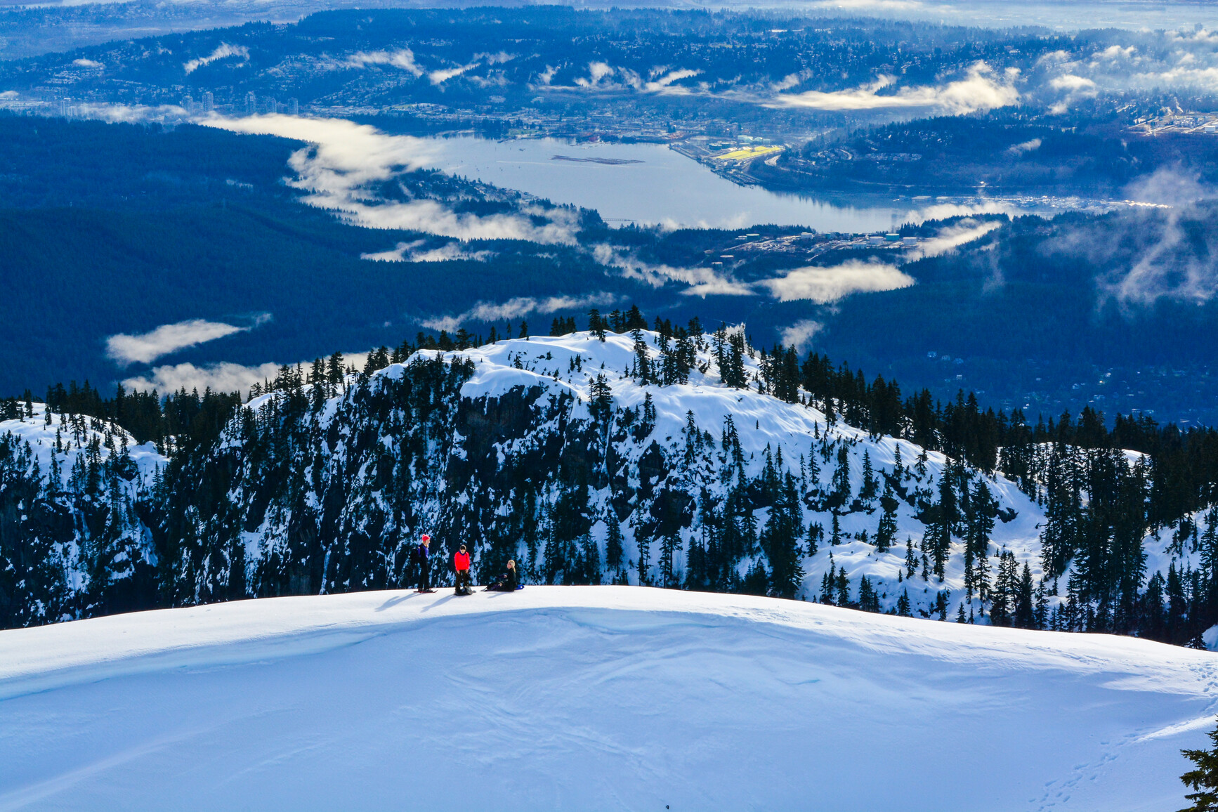 Group of snowshoers at top of snow covered mount over looking Vancouver in the background.