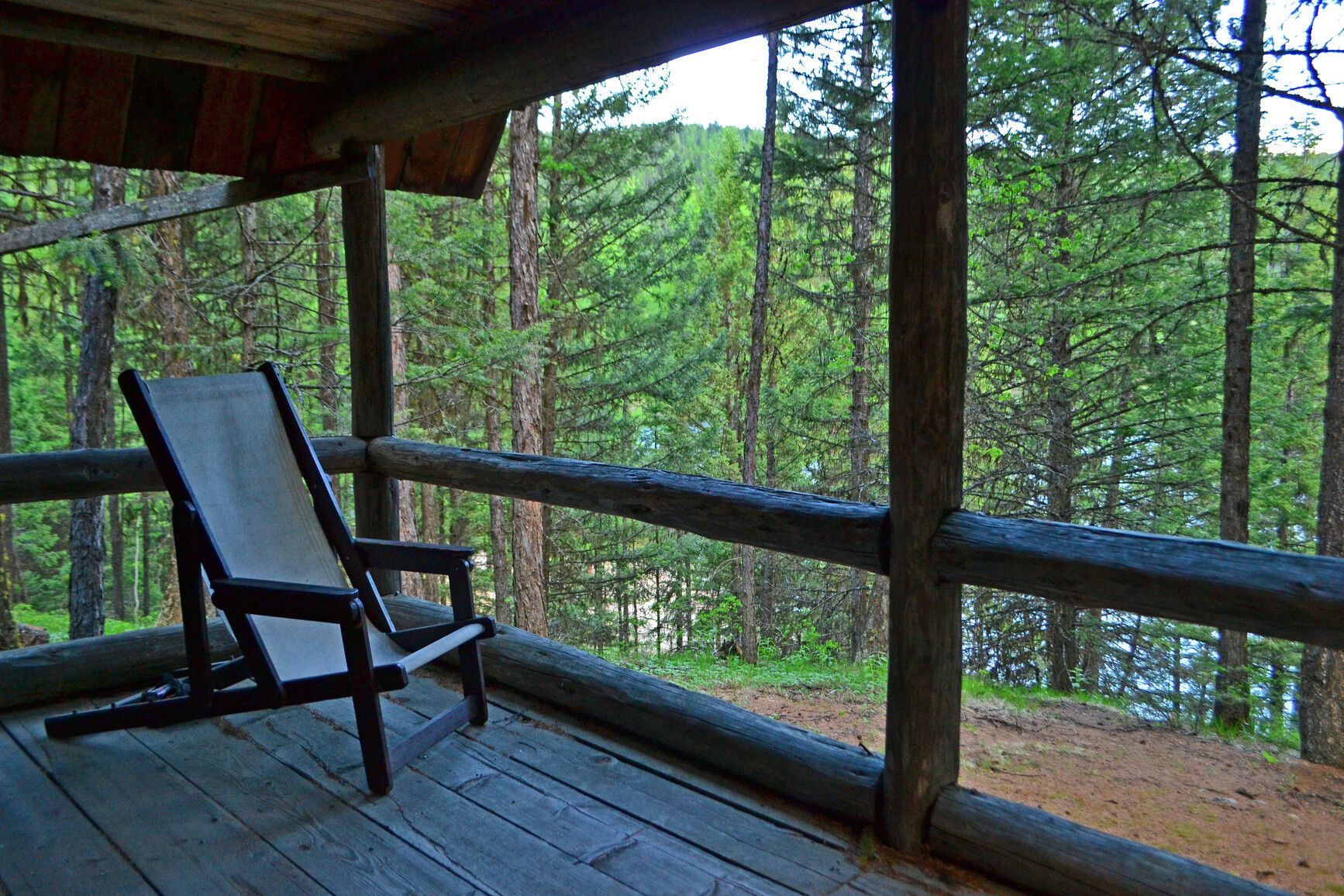 Take in the forest and lake view from the log cabin shelter's deck. A simple wooden chair awaits. Conckle Lake Park.