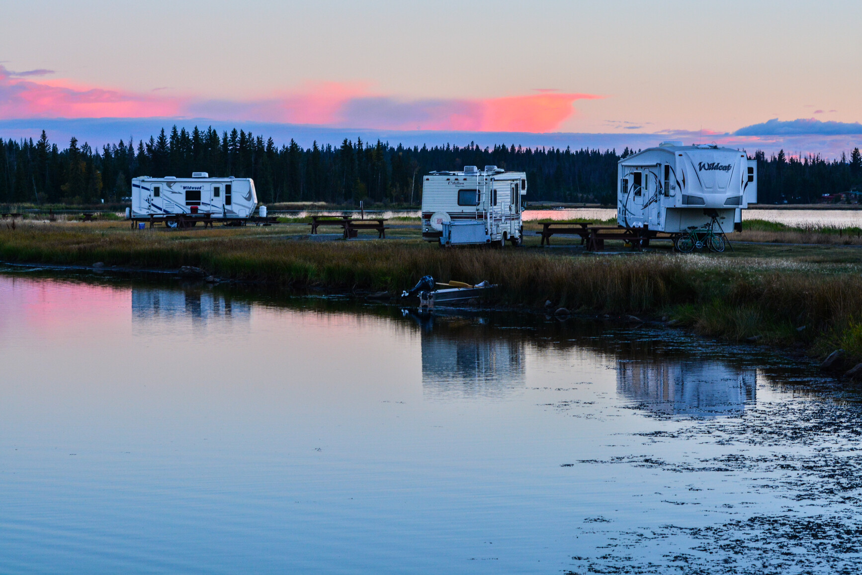Tunkwa Lake - A view of the campground and lake at dusk. Trailers  are in the campground and there is a boat on the shoreline.