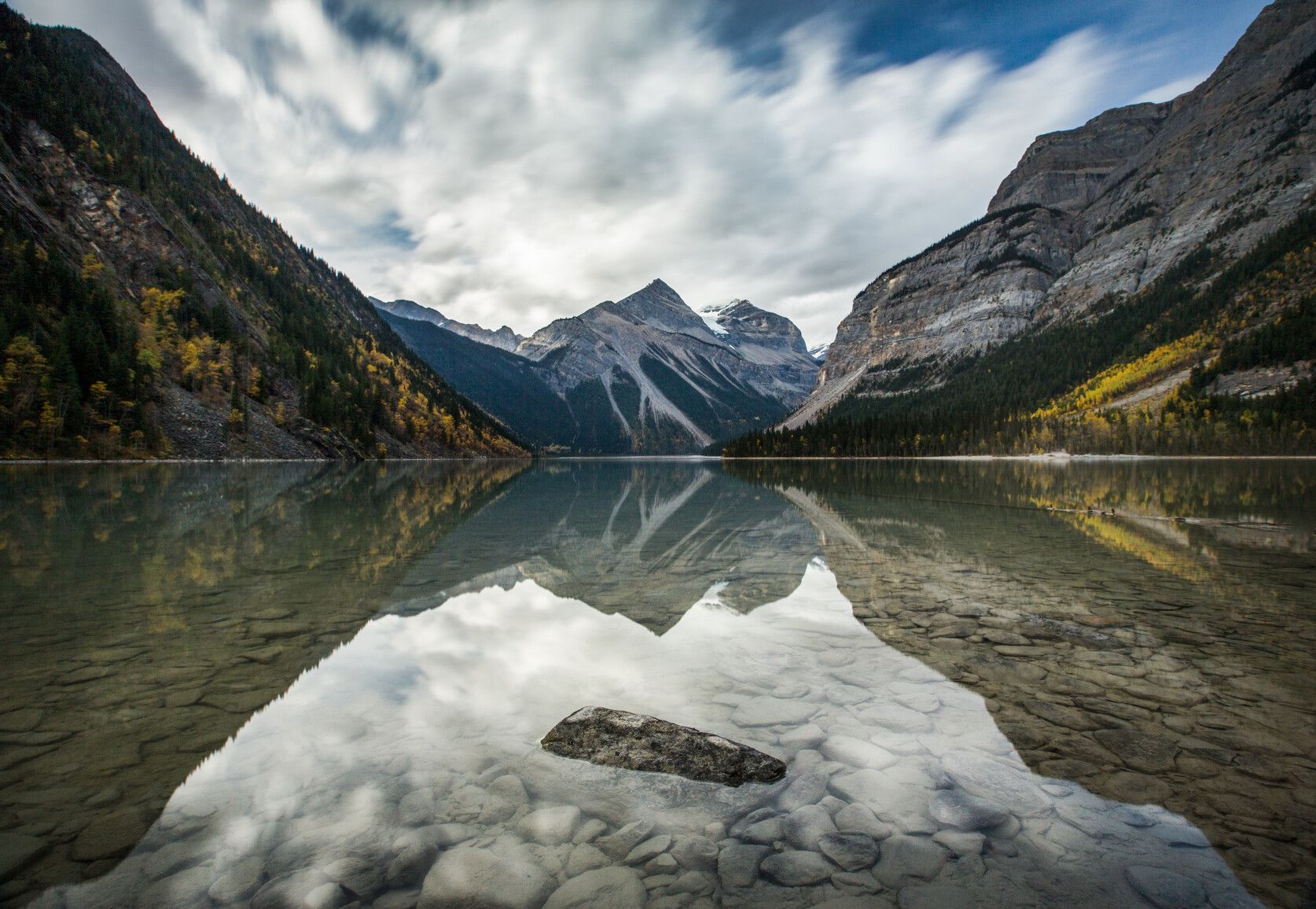 Kinney Lake in fall, with Mount Robson Park's majestic mountains, glaciers, and golden trees mirrored on its serene surface, showcasing nature's breathtaking beauty.