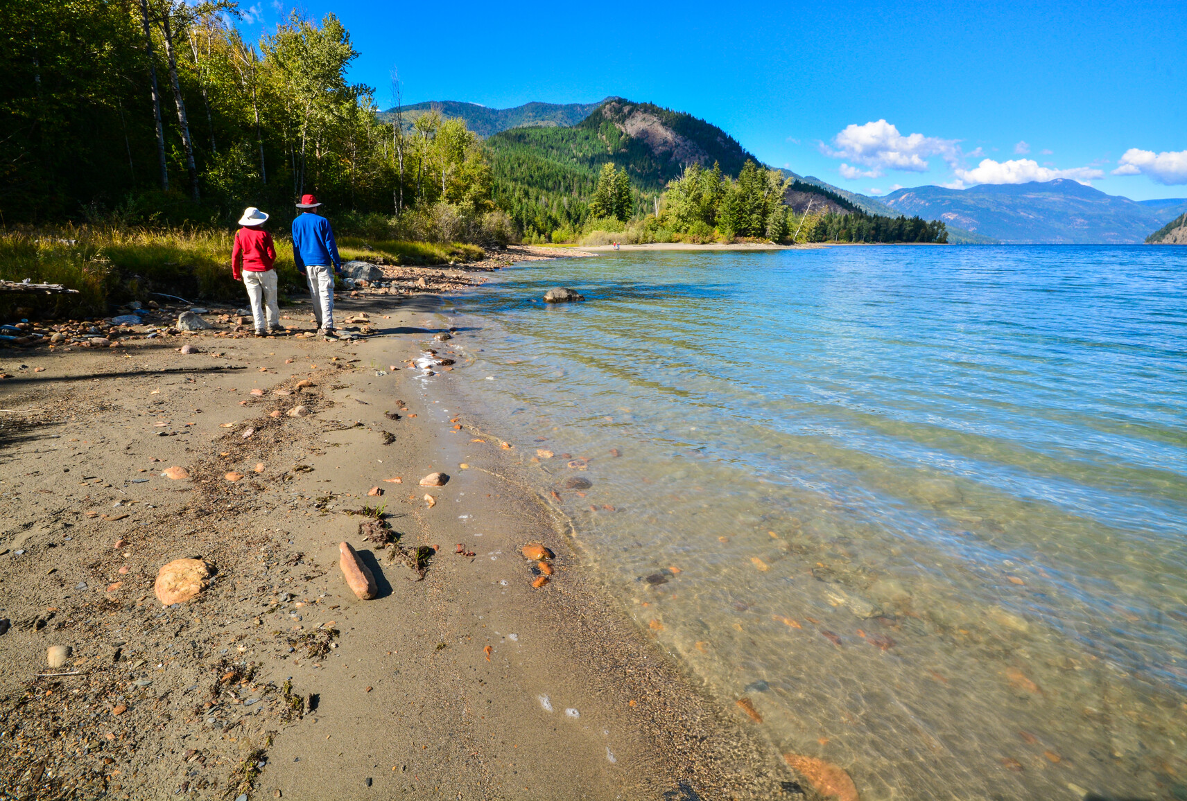 Two park visitors walk along the shore of Adams Lake and enjoy the view of the mountains and forest.