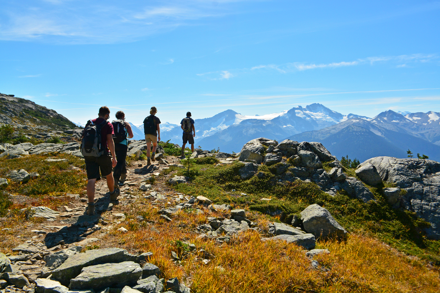 Hikers walking through rocky terrain and mountain views in the background.