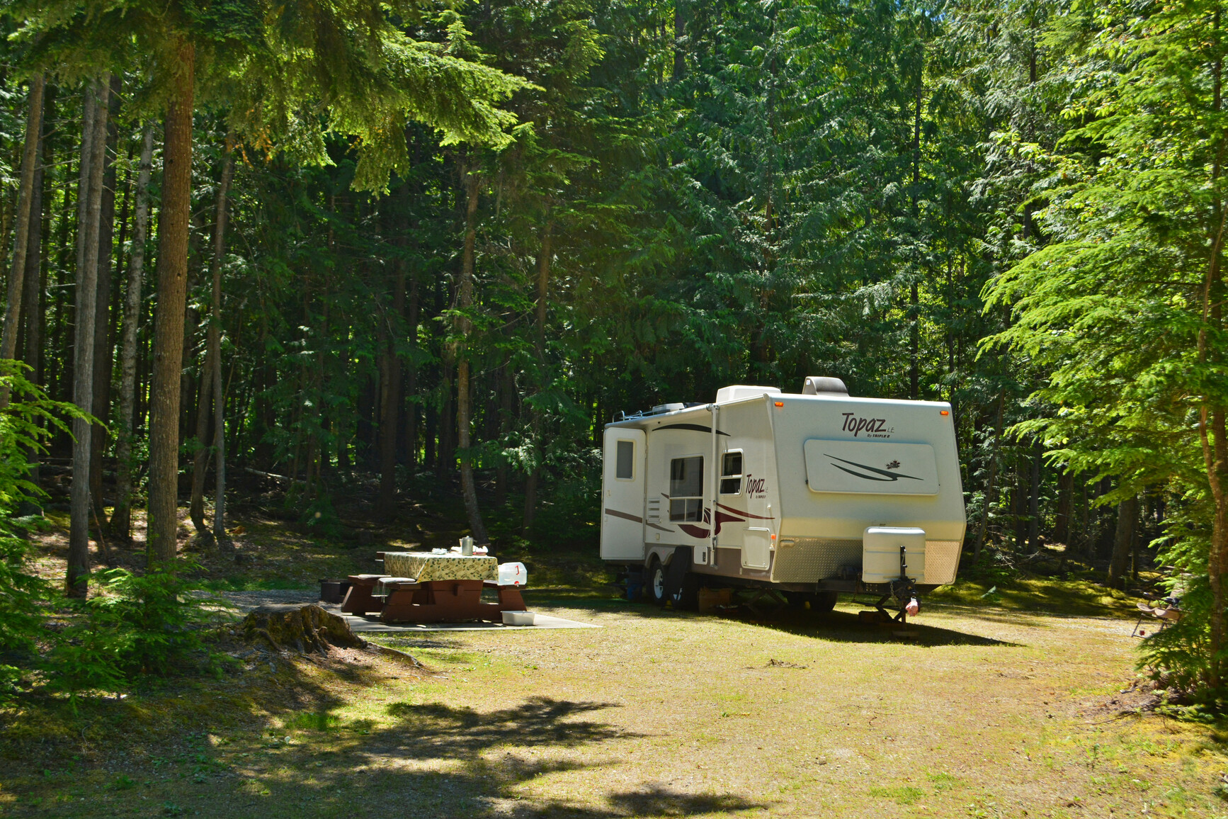 McDonald Creek Park - A campsite with a picnic table, fire ring and trailer. Trees and forest surround the campsite.