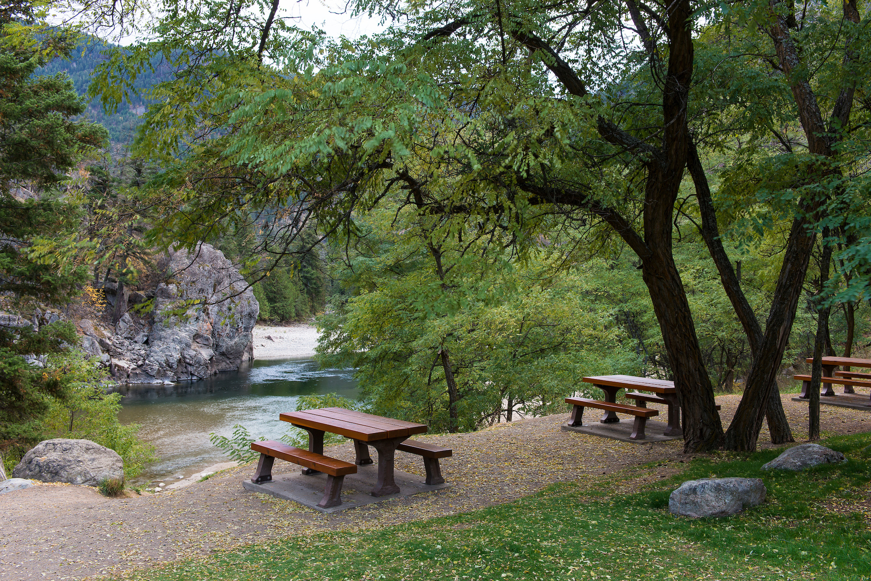 Day use picnic tables set up along the rivers edge underneath tree cover