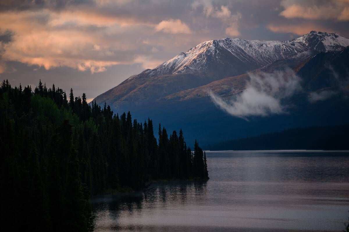 Cold Fish Lake in Spatsizi Plateau Wilderness Park reflects snow-capped peaks and dense forest. The calm water and soft light create a peaceful scene in this remote northern landscape. Courtesy of Destination BC