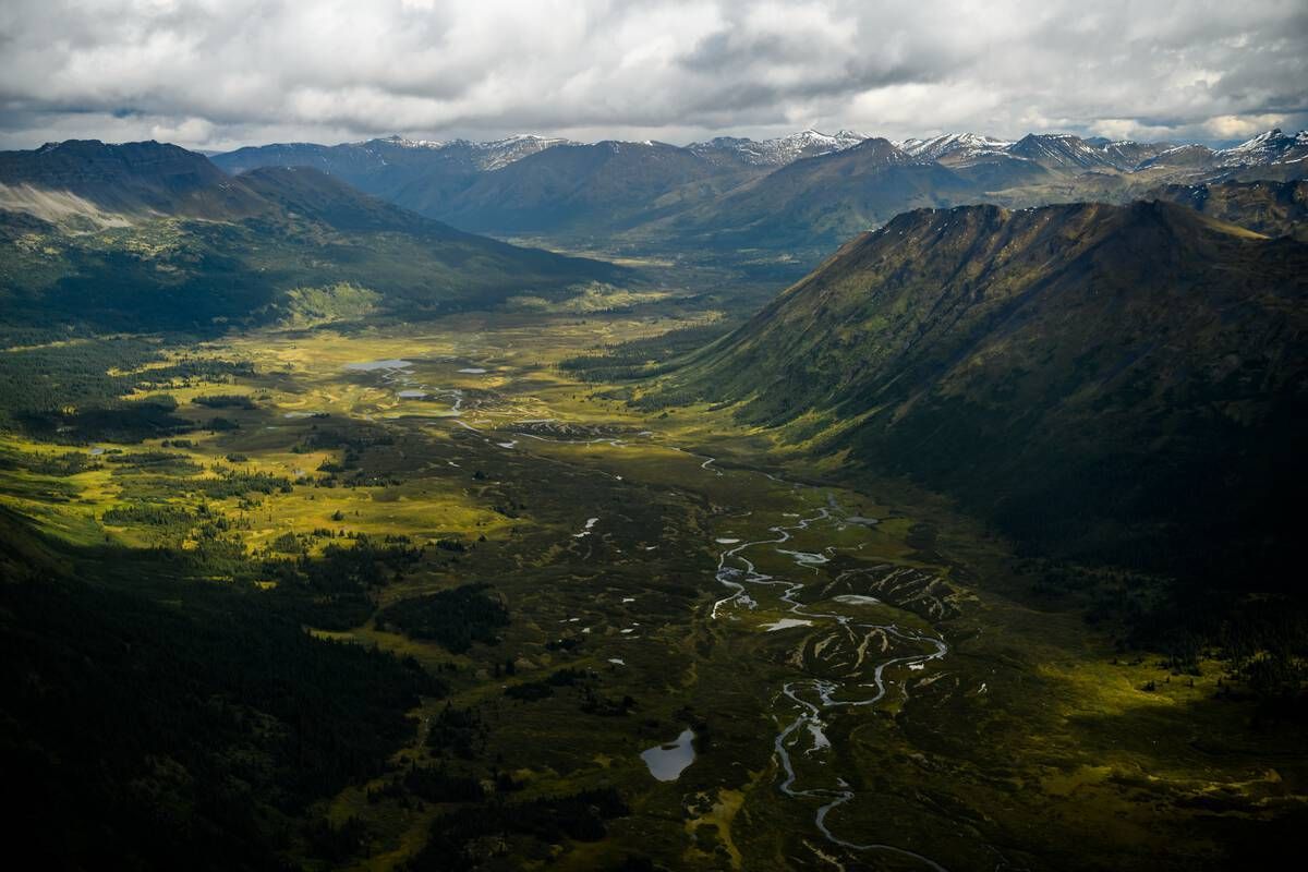 A glacially carved valley in Spatsizi Plateau Wilderness Park cradles a winding river, its broad U-shaped form etched by ancient ice and framed by alpine meadows and distant snowy peaks. Courtesy of Destination BC