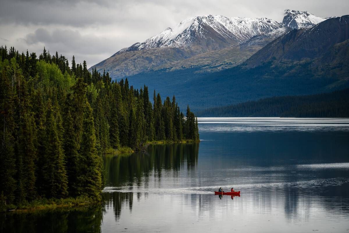 Canoeing at Cold Fish Lake Camp, surrounded by forested shores and snow-capped peaks in the heart of Spatsizi Plateau Wilderness Park. Spatsizi Plateau Wilderness Park