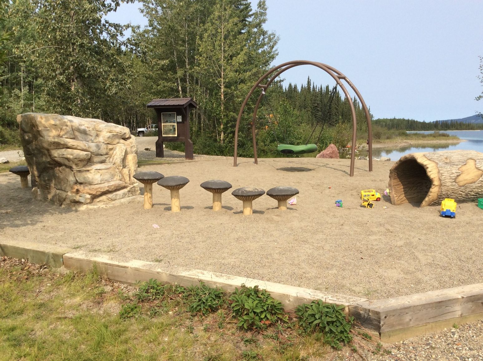 Beside Boya Lake in Tā Ch’ilā Park, a forest playground features stepping stones, a swing, and a log tunnel, offering a fun and scenic spot for families to enjoy the lakeside setting.