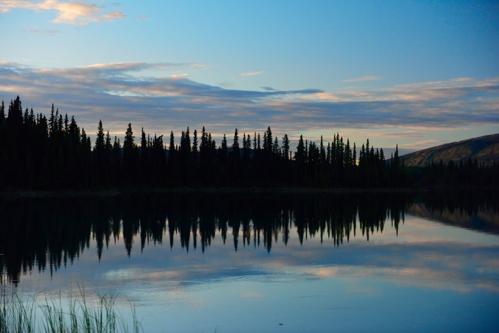 Sunset at Boya Lake in Tā Ch’ilā Park, where the calm water mirrors the azure sky in a tranquil display of light and colour.