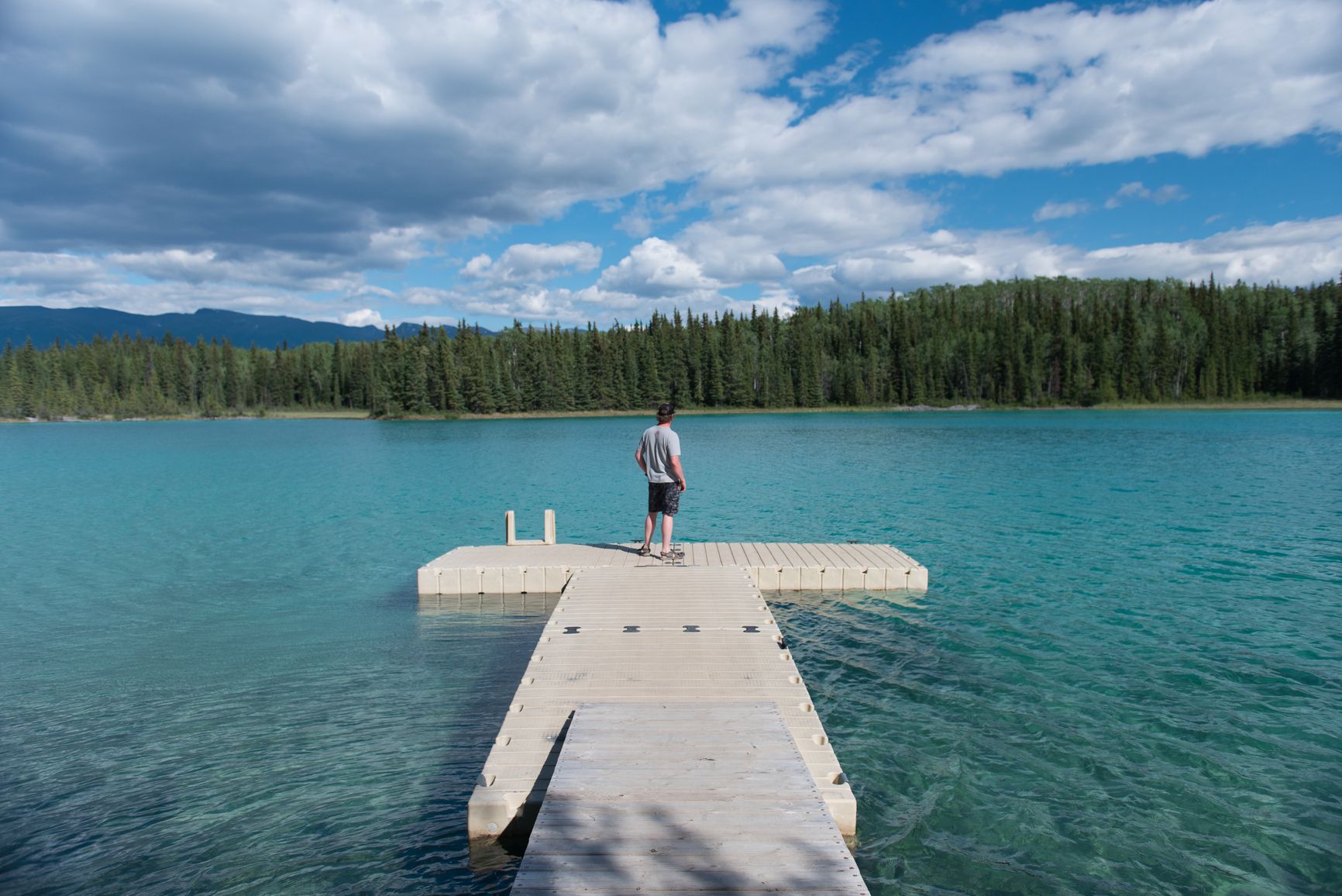 From the dock at Tā Ch’ilā Park, the view opens onto the calm turquoise waters of Boya Lake, with distant mountains rising beyond the forested shoreline.