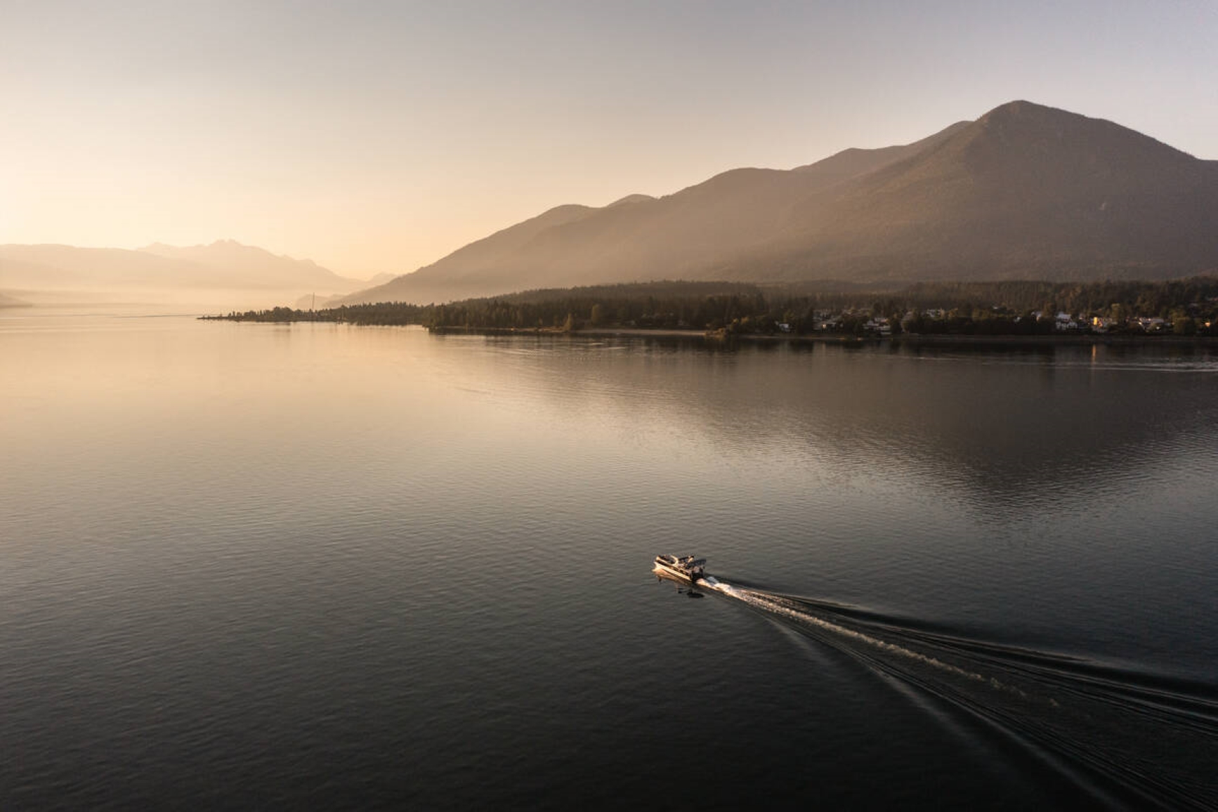 Boat in the lake, with a reflection of the mountain in the distance during sunset. Photo credit: Destination BC