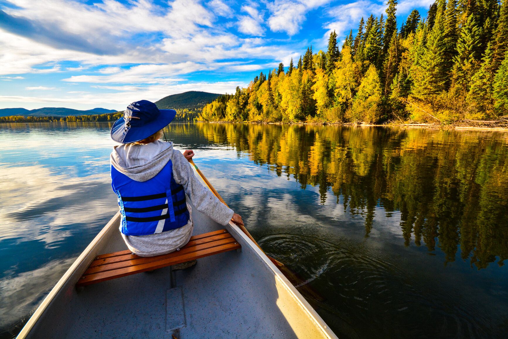 Paddling Bowron Lake as it reflects the vibrant autumn trees, mountains, and forests.