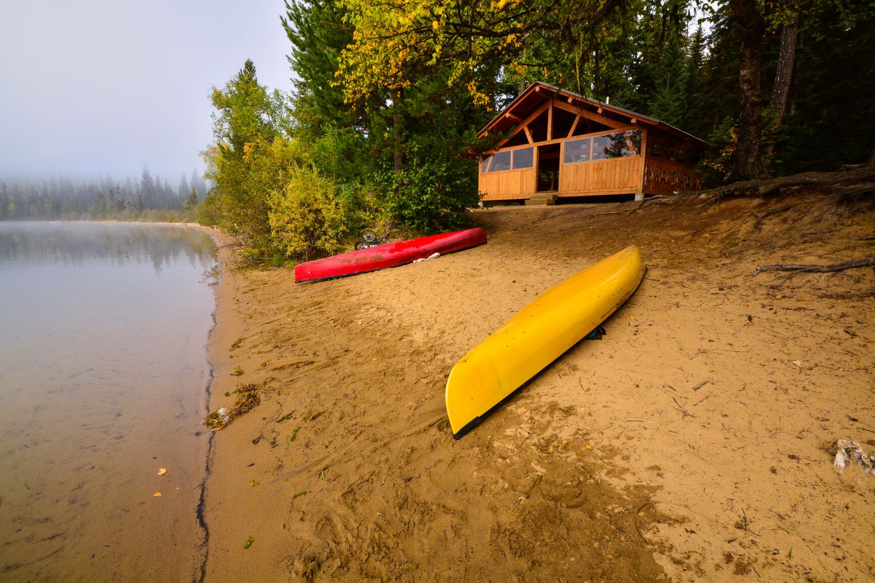 Canoes rest on a beach in front of a cabin on the Spectacle Lakes, part of the Bowron Lakes circuit.