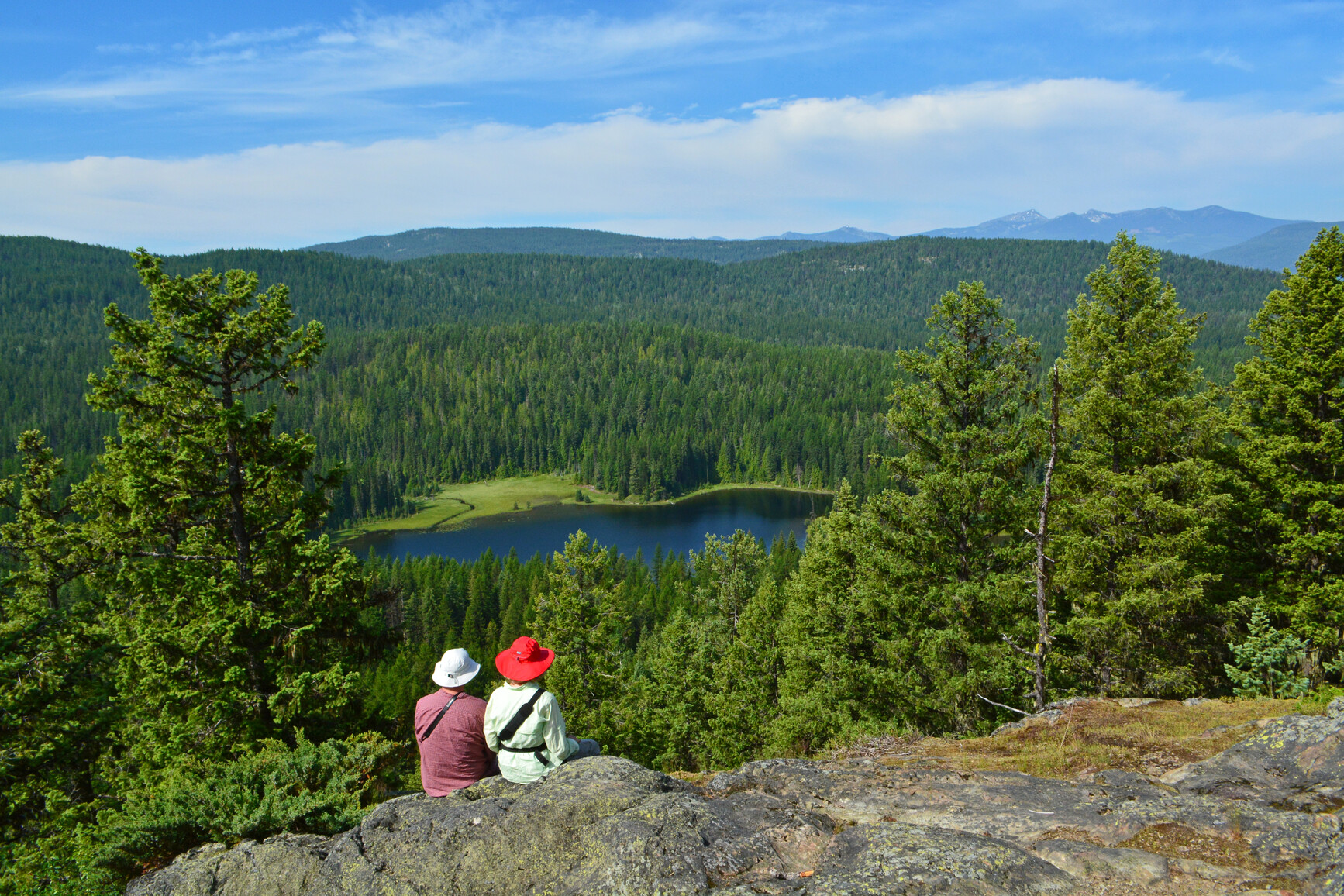 Park visitors hiking on a mountain above Champion Lakes. The lake and surrounding mountains are in view.