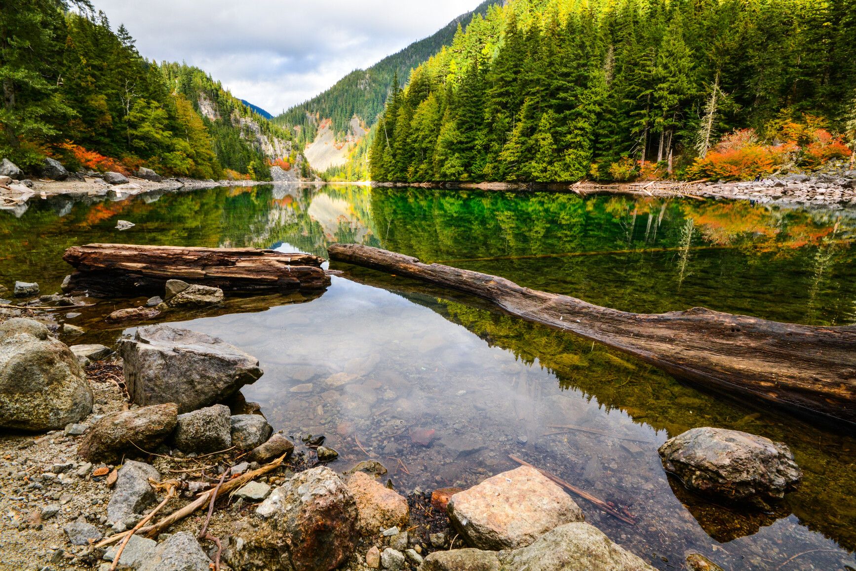 Mountains and autumn forest reflect on the emerald water of Lindeman Lake in Sx̱ótsaqel/Chilliwack Lake Park.