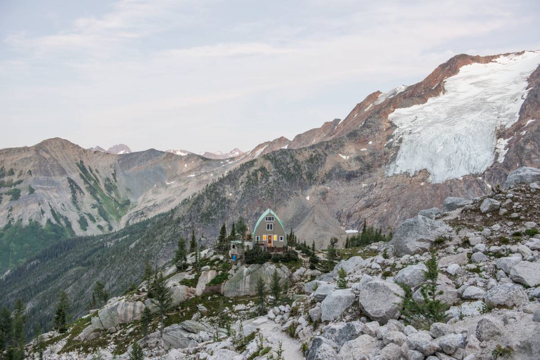 View of cabin perched in between snowcapped mountains and rocky landscape. Photo credit: Destination BC