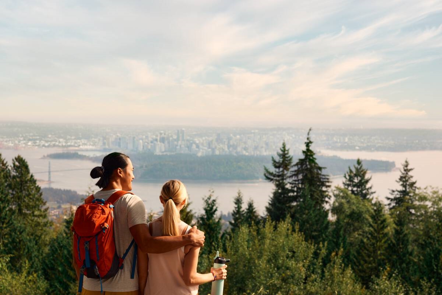 Two park visitors are looking out over to the view of the city in the distance. Photo credit: Destination BC
