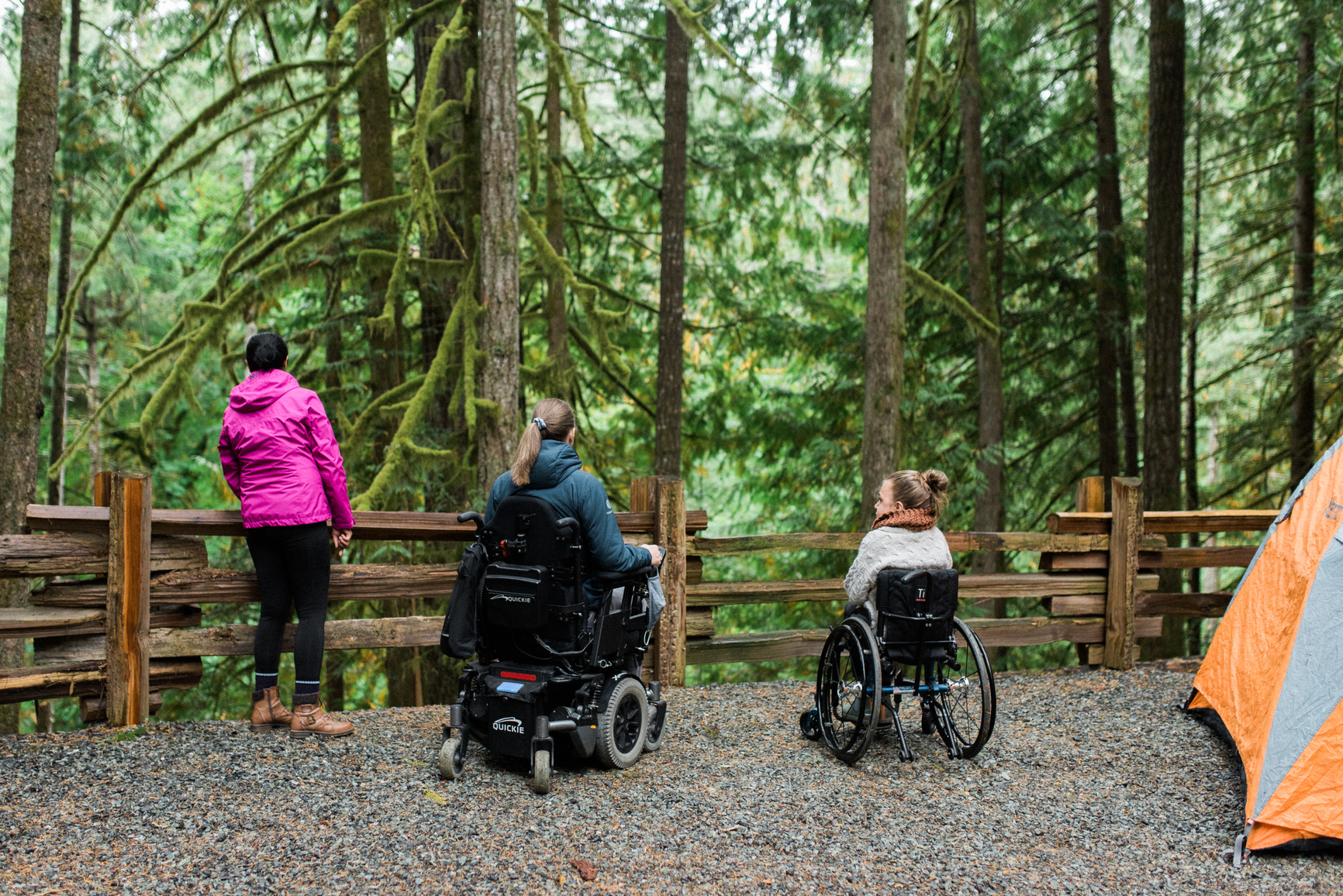 Three visitors, two of whom use wheelchairs, next to their tent