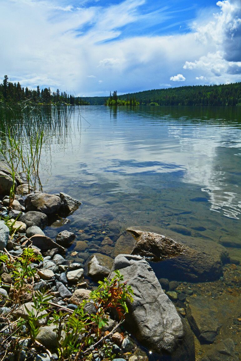 From the rocky shoreline, a view of the blue sky reflecting on the surface of Lac La Hache.