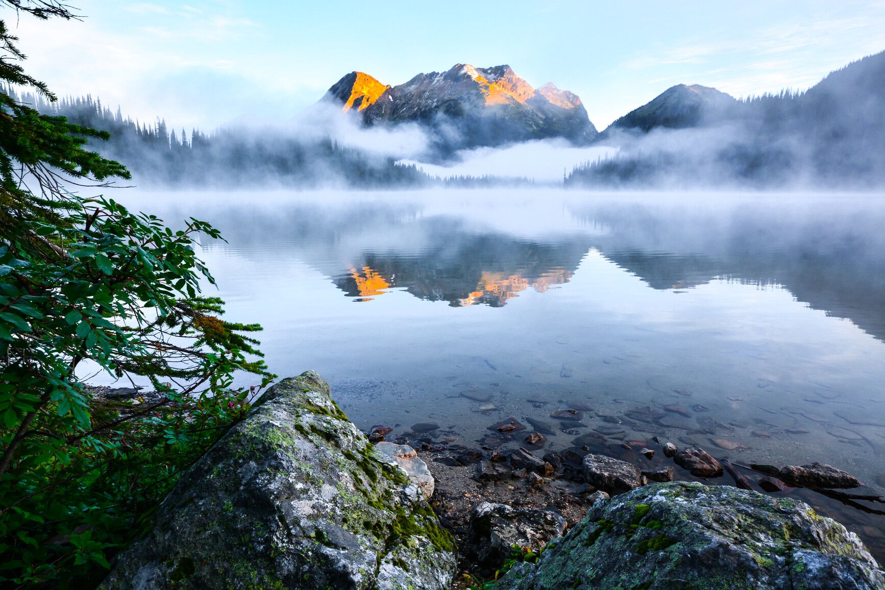 The early morning sun illuminates the peaks as mist rises from Big Peters Lake in Monashee Park.