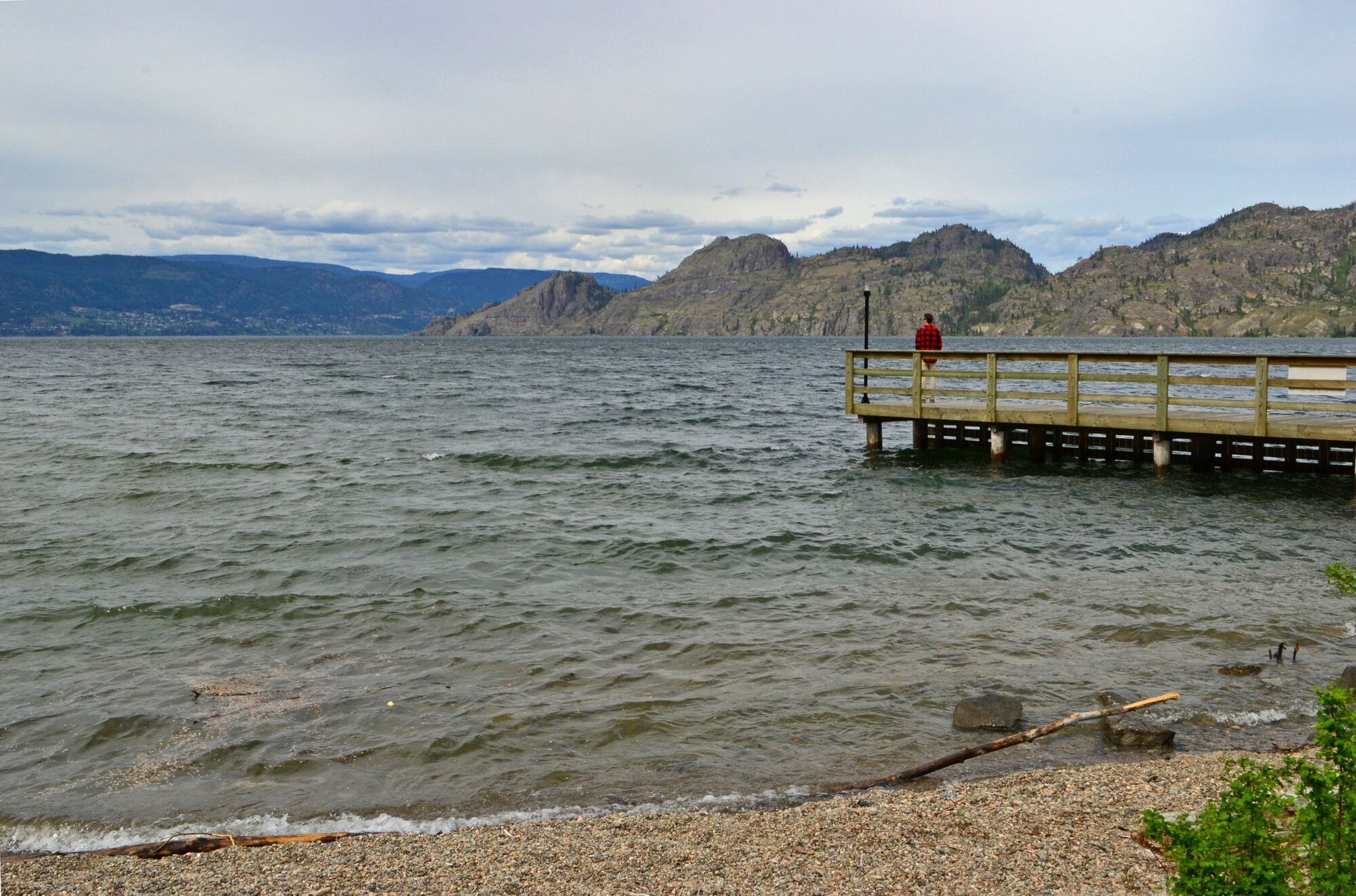 Lake waves crash on shore while someone overlooks the mountains from the dock