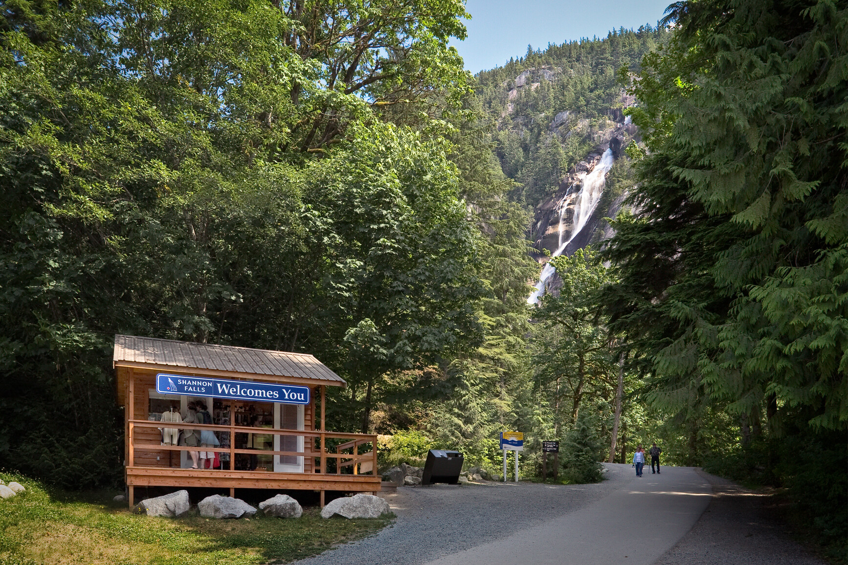 View of falls cascading down the mountain. Park visitors on trail and at kiosk in the foreground.