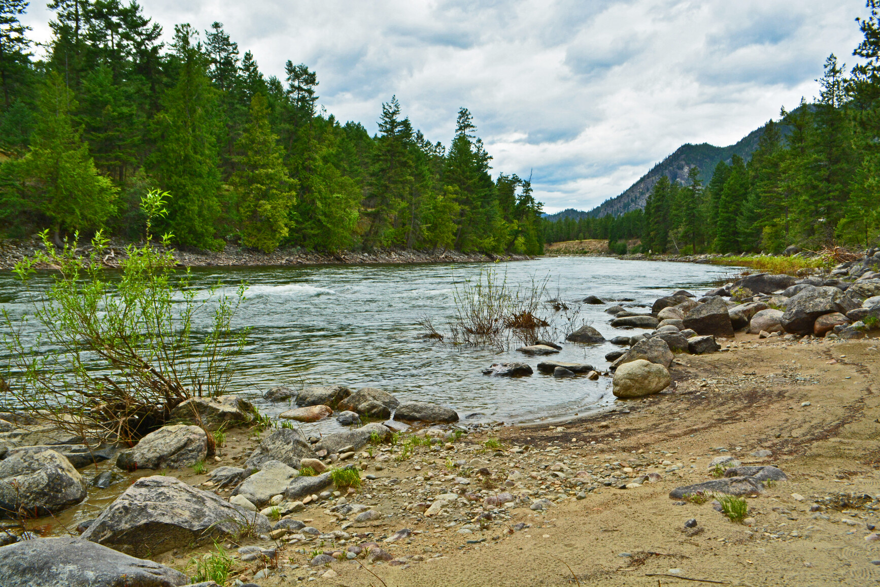 Similkameen River - A rocky shoreline with trees, forest and mountains in the background.