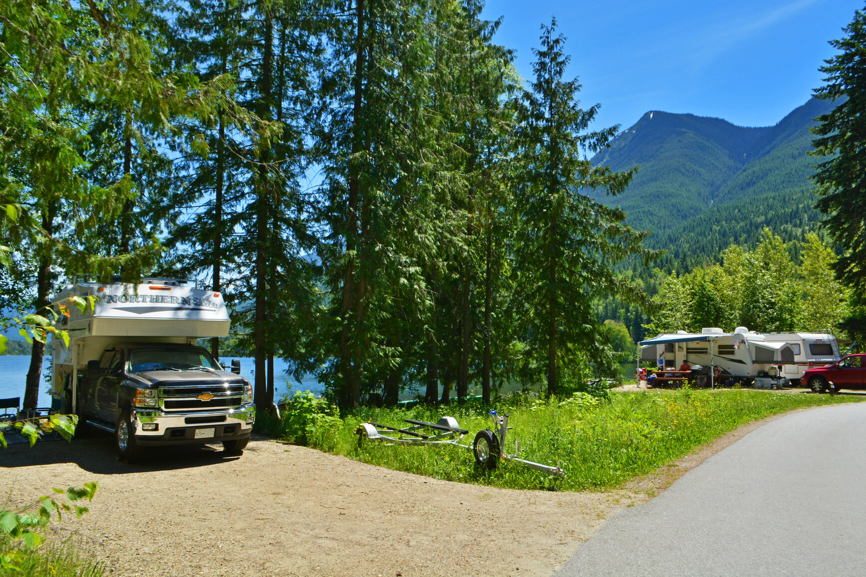 Summit Lake Park campground. Trailers and vehicles are in lakeside campsites. The lake and mountains are in the background of the campsite.