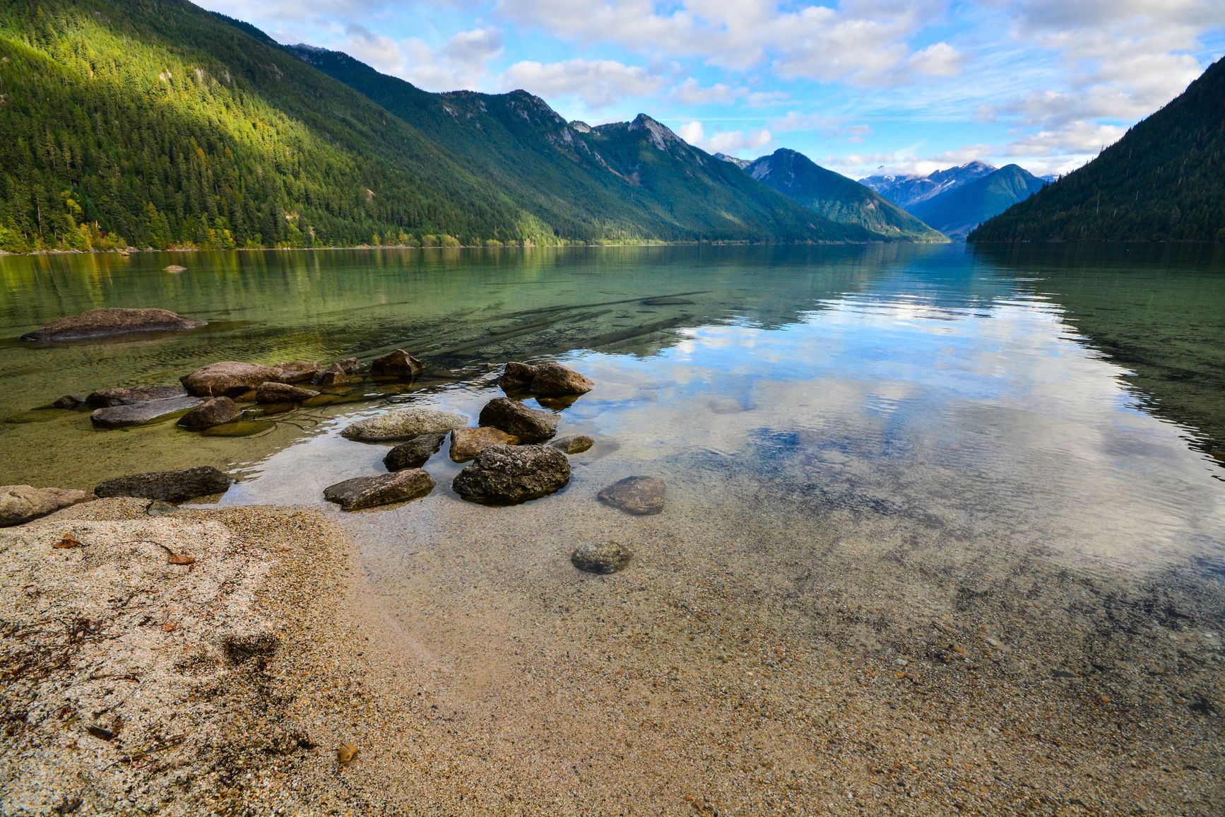 View of the forest-covered mountains from the shoreline. Sx̱ótsaqel/Chilliwack Lake Park.