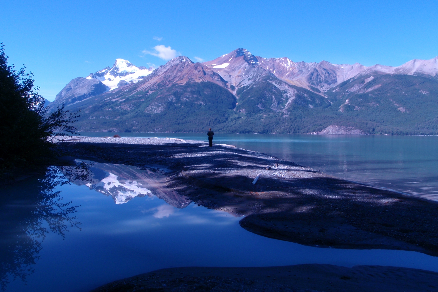 A camp visitor walking along the shoreline with mountains in the background