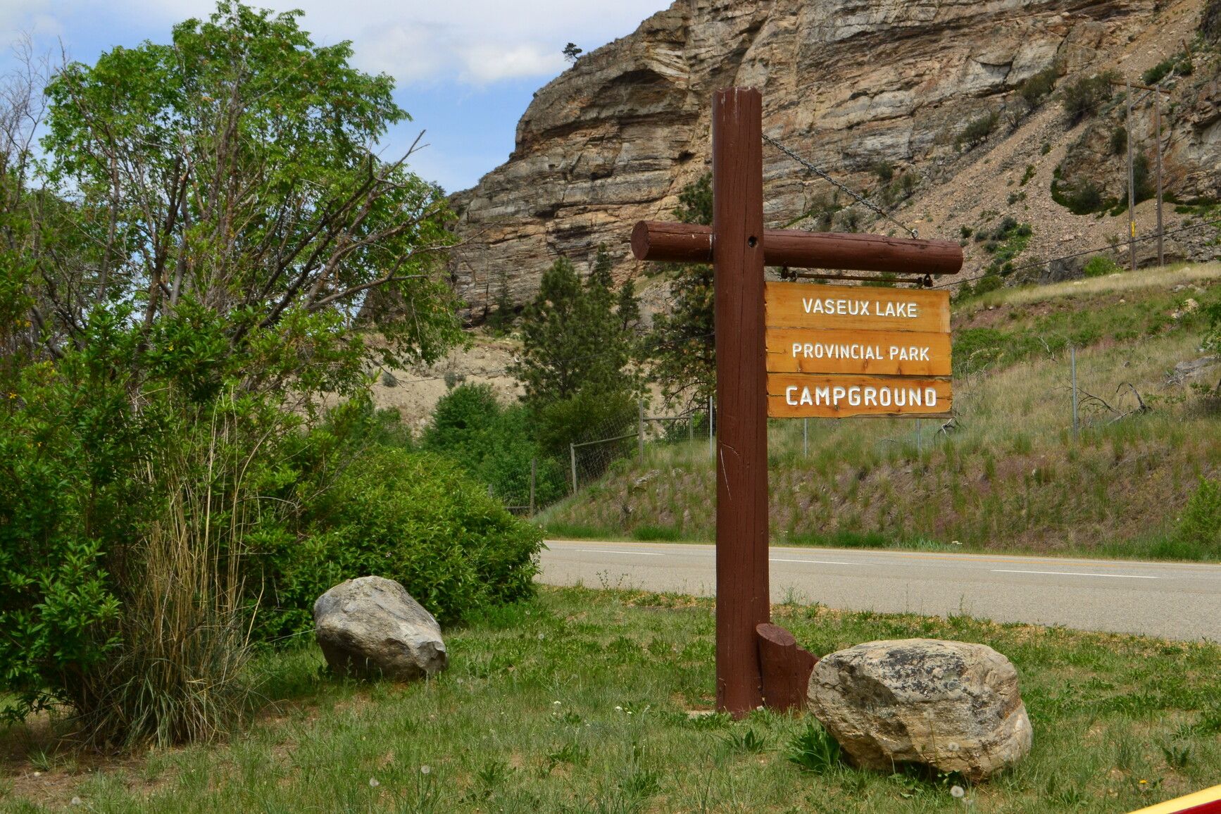 Set against the backdrop of rugged sedimentary rock formations on a mountain, the entrance sign of Vaseux Lake Park proudly welcomes visitors.